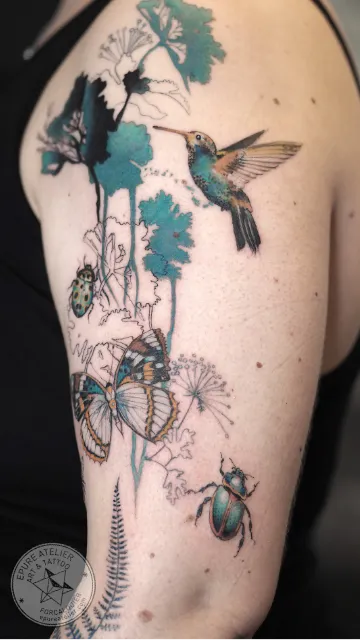 Tatouage colibri avec scarabée, papillon et éléments botaniques sur le bras
